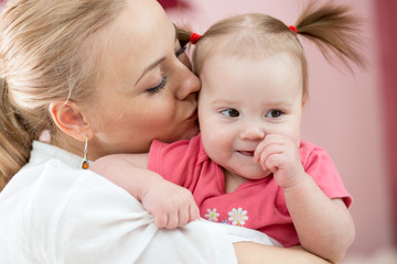 Portrait of happy mother kissing her baby daughter at home