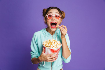 Photo of hipster girl 20s in sunglasses screaming and holding bucket with popcorn, isolated over...