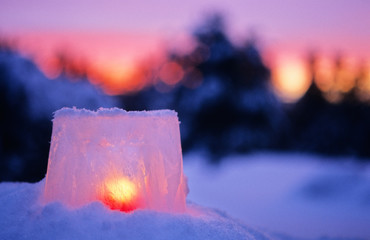 Ice lantern in snowy landscape at dusk. Christmas time.