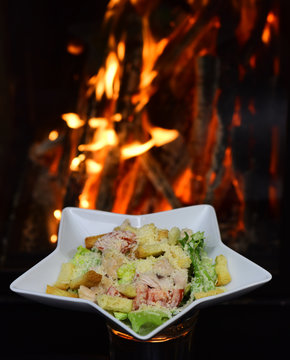 Classic salad with grilled chicken on burning fire background. Caesar salad with chicken meat. Deliciousness jumping into the mouth