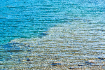 crystal clear blue cool water at the shore of a wild lake in a quarry without people with steep rocky beaches and large boulders on a summer warm day
