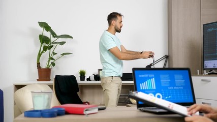 Man playing a video game on the console while her partner is working on the computer in the same room looking at company data and analysis in animated chart. Rack focus dolly slider footage - Powered by Adobe
