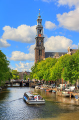 Canalboat tour at the UNESCO world heritage Prinsengracht canal with the Westerkerk (Western church) on a sunny summer day with blue sky and clouds - obrazy, fototapety, plakaty