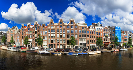 Fototapeta premium Piękna panoramiczna panorama liniowa kanału Prinsengracht, wpisanego na listę światowego dziedzictwa UNESCO, w Amsterdamie, w Holandii, w słoneczny letni dzień z błękitnym niebem i chmurami