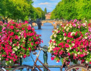 Naklejka premium Piękne, żywe letnie kwiaty i rower na moście nad słynnymi kanałami światowego dziedzictwa w Amsterdamie w Holandii