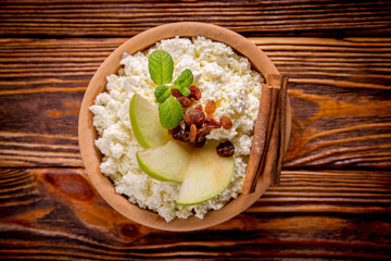 homemade cottage cheese in a wooden bowl, mint, raisins, cinnamon, apples lie on a wooden table