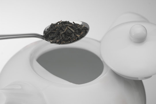 spoon with tea leaves and a white ceramic teapot, macro shooting