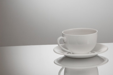 one white cup and saucer on a light background with reflection