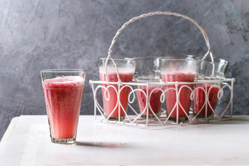 Red fruit berries watermelon iced cocktail in glasses stand on white marble table with grey wall at background. Summer cold drink.
