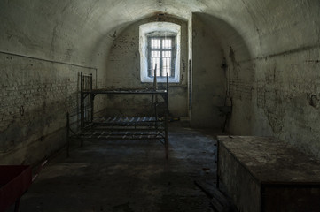 Fototapeta na wymiar Old prison cell/abandoned prison cell with metal bunk beds and sitting platform and steel bars at the small window.
