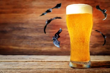 Foto auf Leinwand Glas kaltes helles Bier mit fliegenden Fledermäusen auf Holzhintergrund für Halloween © nata_vkusidey