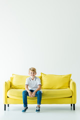 smiling adorable boy sitting on yellow sofa and looking at camera on white