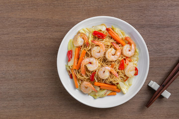 top view of hot and spicy stir fried instant noodle with shrimp and vegetable in a ceramic dish on wooden table. asian homemade style food concept.