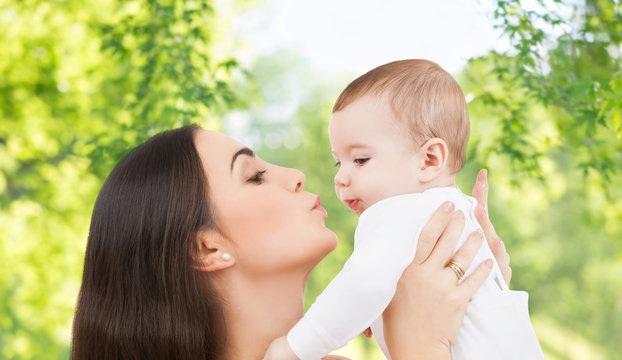 family and motherhood concept - happy smiling young mother kissing little baby over green natural background