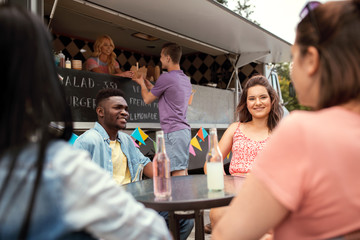 leisure and people concept - happy friends with drinks sitting at table at food truck