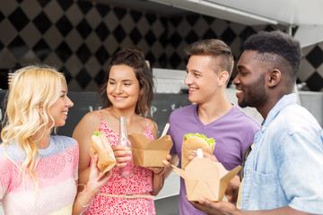 leisure and people concept - happy friends with drinks eating and talking at food truck