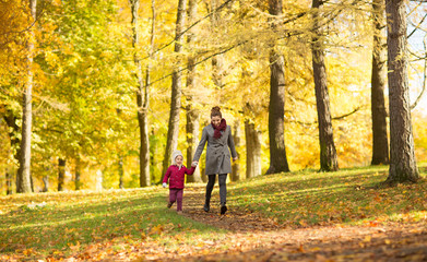 Fototapeta premium family, season and people concept - happy mother and little daughter walking along autumn park