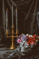 silver skull with flowers and candelabrum with candles on black cloth with spider web for halloween