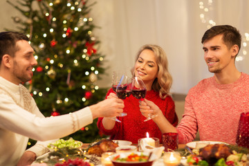 holidays and celebration concept - happy friends having christmas dinner at home, drinking red wine and clinking glasses