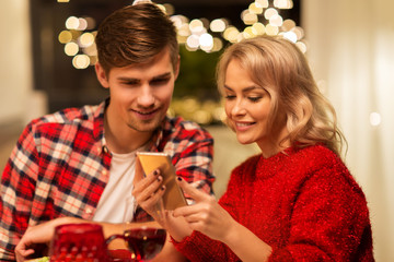 holidays, technology and celebration concept - happy couple having christmas dinner at home and using smartphone