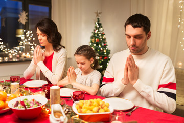 holidays, family and celebration concept - happy mother, father and little daughter having christmas dinner and praying before meal at home