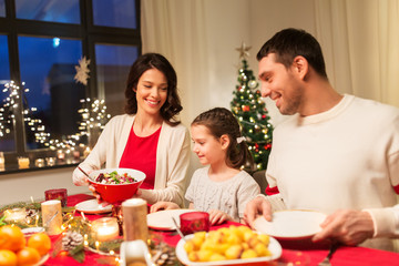 holidays, family and celebration concept - happy mother, father and little daughter having christmas dinner at home