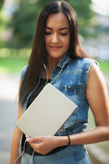Young pretty brunette girl with the tablet and listening to music on the street in summer.