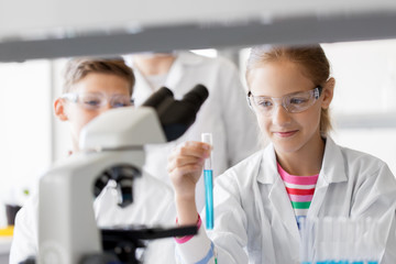 education, science and children concept - teacher and students with test tubes studying chemistry...