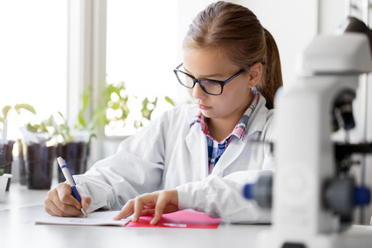 education, science and children concept - girl studying chemistry at school laboratory and writing to workbook