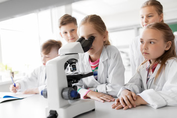 education, science and children concept - kids or students with microscope studying biology at...