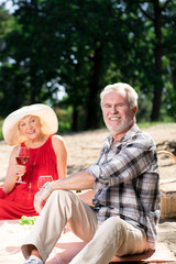 Romantic picnic. Cheerful confident aged man smiling while having a picnic with his happy wife