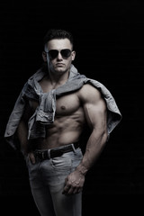 Fototapeta na wymiar Handsome Young Man With Sexy Fit Body Posing On Dark Background Indoors. Closeup Portrait Of Healthy Strong Male With Perfect Body Shape And Muscular Abs. Bodybuilding Concept.