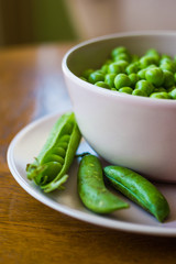 pink bowl with green peas and three pea pods lie near