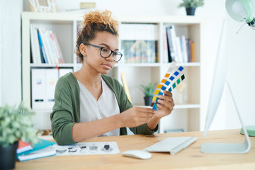 Portrait of young African-American woman holding swatches while choosing color scheme  in design agency - Powered by Adobe