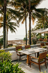 Fototapeta premium Dinner table and chairs under umbrella in tropical coconut tree garden, Phuket Thailand