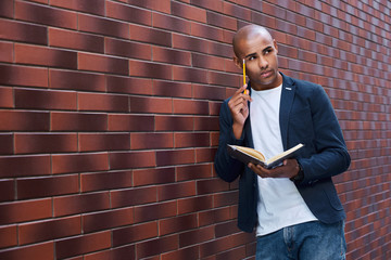 Brain development. Young guy standing on wall reading book touching head with pencil thinking