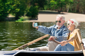 Selfie. Positive progressive elderly couple relaxing in the boat and taking selfies