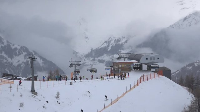 Establishing shot of mountain stations of lifts in a skiing resort with heavy snowfall rolling in, covering most of the beautiful alpine mountain panorama.