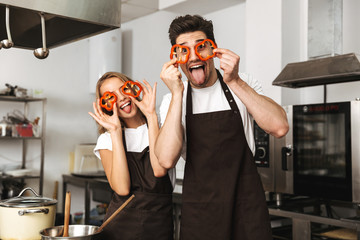 Excited young friends loving couple chefs on the kitchen cooking having fun covering eyes with...
