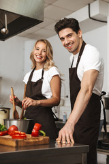 Smiling excited young friends loving couple chefs on the kitchen cooking.