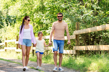 Obraz premium family, leisure and people concept - happy mother, father and little daughter walking in summer park