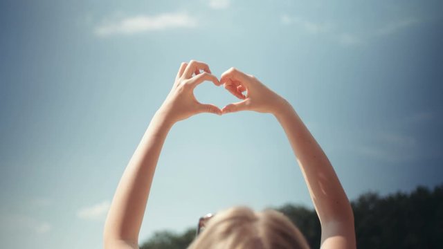 Young woman rising hands to a sky in shape of heart.