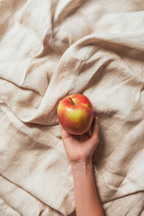 cropped view of woman holding apple on beige sacking cloth