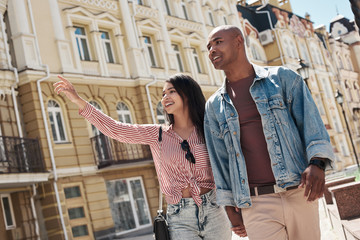 Romantic Relationship. Young diverse couple walking on the city street holding hands sightseeing smiling happy - Powered by Adobe