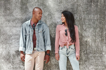 Couple shoot. Young diverse couple standing on the city street on wall looking at each other smiling happy