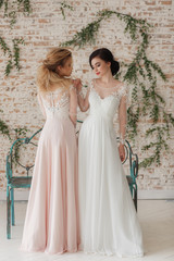 Full length portrait of two attractive young women in wedding dresses on rustic brick wall background. Gay lesbian concept