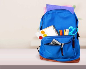 Colorful school supplies in backpack on blackboard background