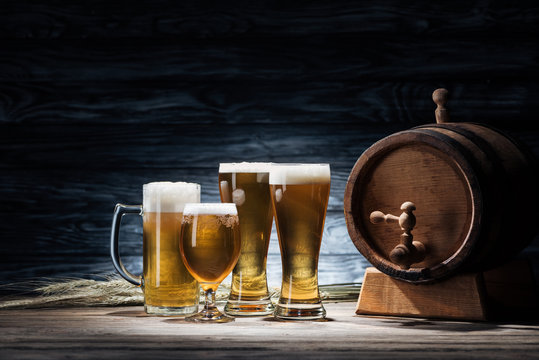 glasses of tasty beer, wheat spikelets and beer barrel on wooden table, oktoberfest concept