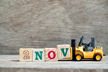 Toy forklift hold block V to complete word 2nov on wood background (Concept for calendar date 2 in...