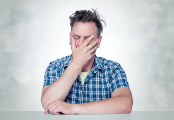 Facepalm man, Portrait male in plaid shirt sitting at a table, epic fail emotion.